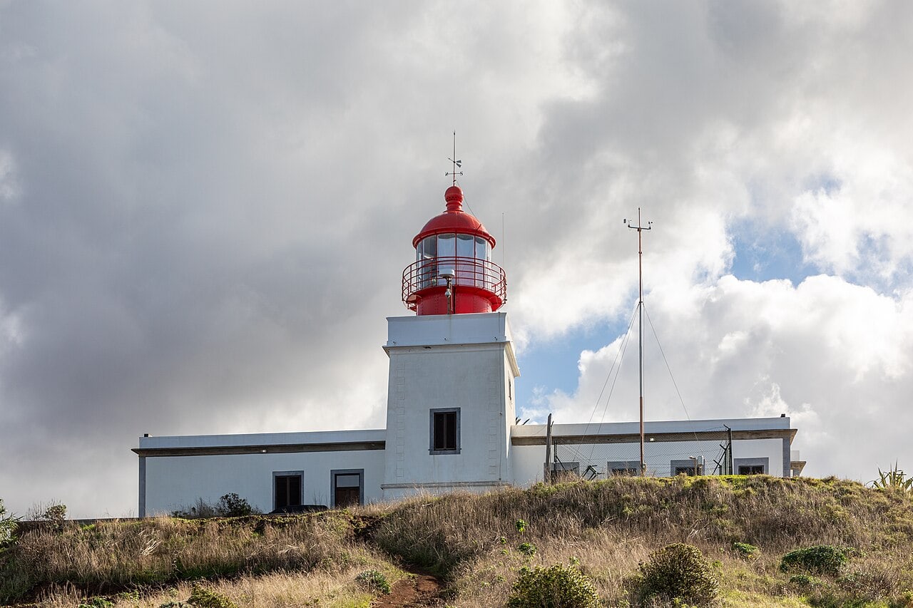 The red-topped lighthouse at Ponta do Pargo beside grassy ground on the approach to the viewpoint.